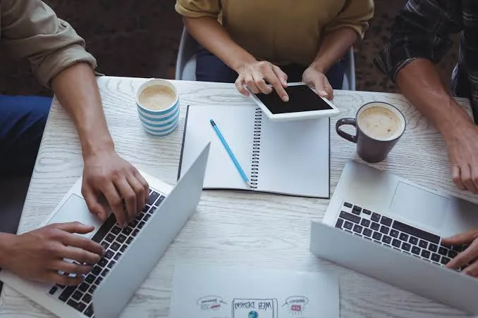 Team collaborating at a desk with laptops and coffee.